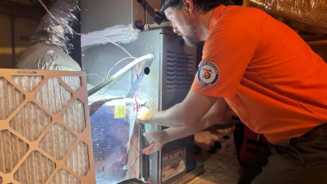 HVAC technician performing maintenance on an indoor furnace system, inspecting internal components during a scheduled heating system service