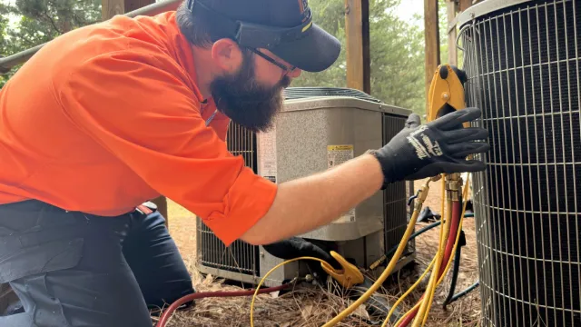HVAC technician performing maintenance on an outdoor air conditioning condenser unit as part of a scheduled cooling system service