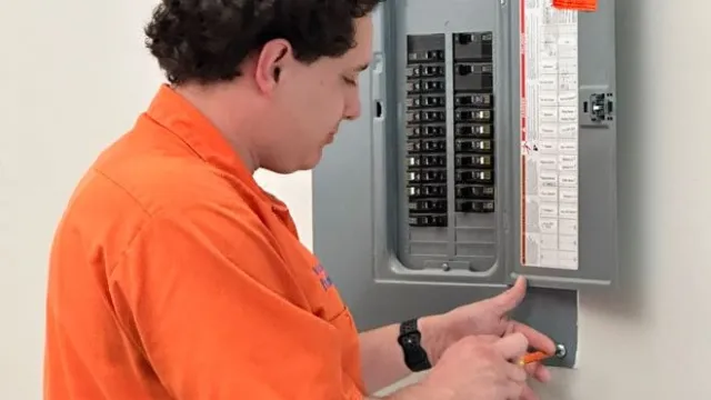 An electrician in an orange shirt installing a circuit breaker in an electrical panel.