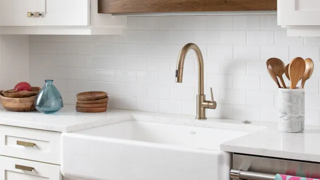 Modern kitchen sink with brass faucet, white tile backsplash, wooden shelves, and colorful LOVE towel on dishwasher