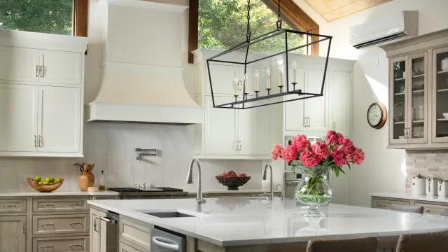 Bright modern kitchen with white cabinetry, marble island, large windows, and pink flowers in vase on counter.