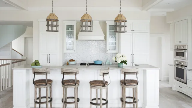 Bright modern kitchen with white cabinetry, four wooden bar stools, marble island, and three hanging pendant lights.