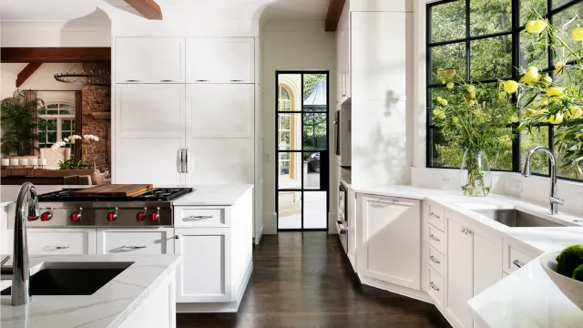 Bright modern kitchen with white cabinetry, marble countertops, stainless steel appliances, and large black-framed windows.