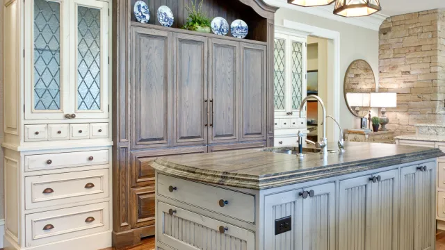 Bright rustic kitchen with wooden island, blue patterned cabinets, hanging lantern chandelier, and hardwood floors.