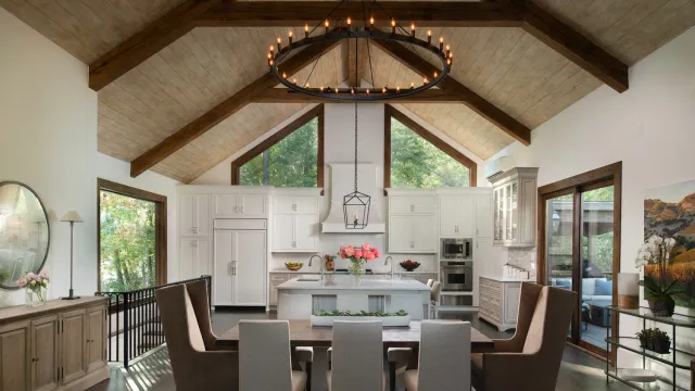 Spacious kitchen and dining area with vaulted ceiling, wooden beams, white cabinetry, and modern lighting.