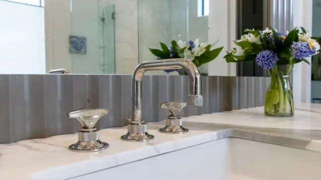 Modern bathroom faucet with stylish design and floral arrangement in the background.