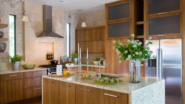 Modern kitchen with wooden cabinets, granite island, stainless steel appliances, and fresh flowers in a glass vase.