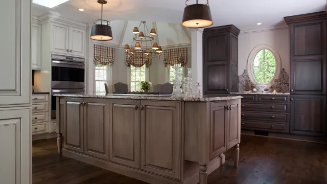 Spacious kitchen with central island, wooden cabinets, hanging lights, and round window providing natural light.