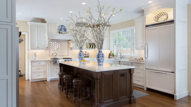 Bright modern kitchen with white cabinetry, dark wood island, marble countertop, and decorative blue vases with branches.