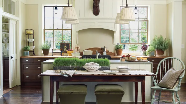 Bright kitchen with wooden floors, green stools, plants, a wooden table, and large windows letting in natural light