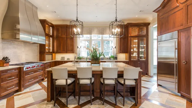 Spacious kitchen with wooden cabinets, large island with five chairs, stainless steel appliances, and pendant lights.