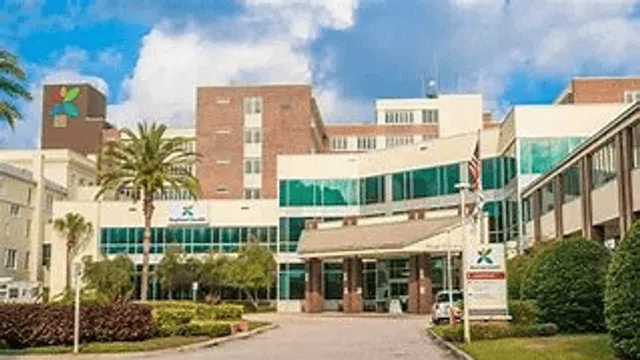 Modern hospital building with glass windows, palm trees, and a clear blue sky in the background