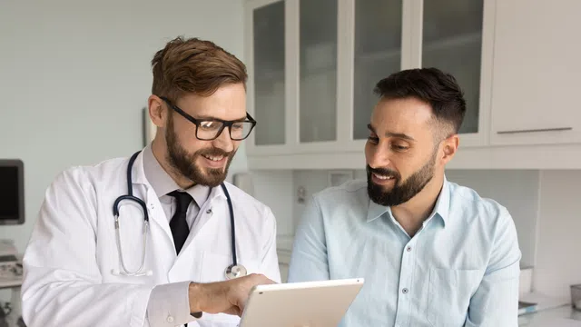 Doctor with stethoscope showing patient information on tablet during consultation in clinic room.
