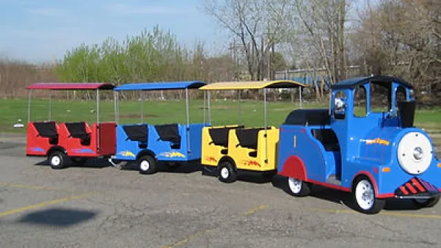 Colorful miniature train train ride for children parked outside on pavement with green grass background