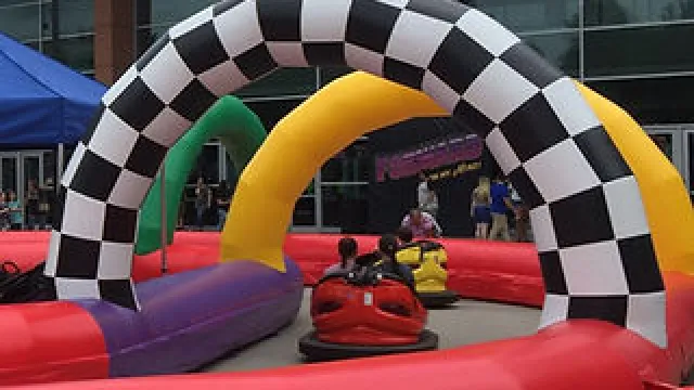 Children riding bumper cars on a colorful inflatable racetrack with checkered archways and tents nearby