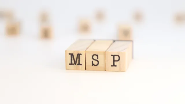 Wooden blocks with letters MSP in focus on a white surface with blurred blocks in the background.