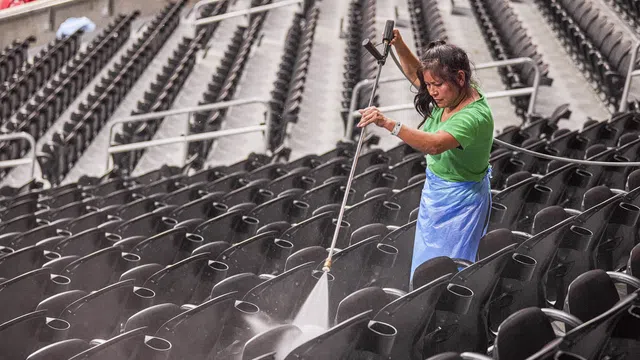Woman in green shirt pressure washing rows of black stadium seats with water spray.