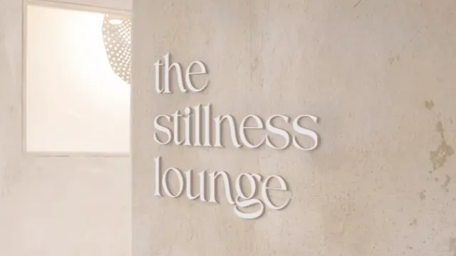 Minimalist beige wall with soft shadows and the words 'the stillness lounge' in elegant lettering.