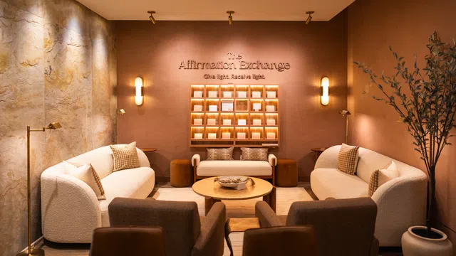 Warm cozy lounge with beige sofas, round wooden coffee table, modern lighting, and Affirmation Exchange sign.