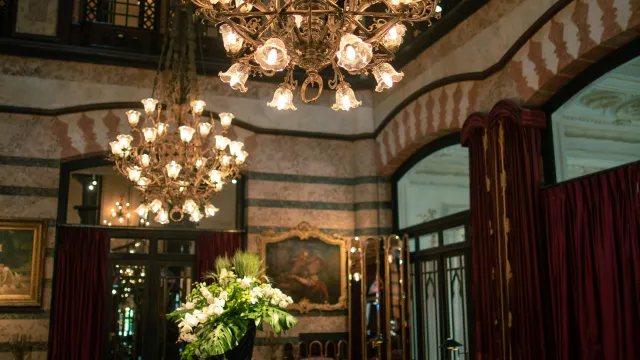 Elegant room with ornate chandeliers, floral centerpiece on table, plush seating, and classic decor.