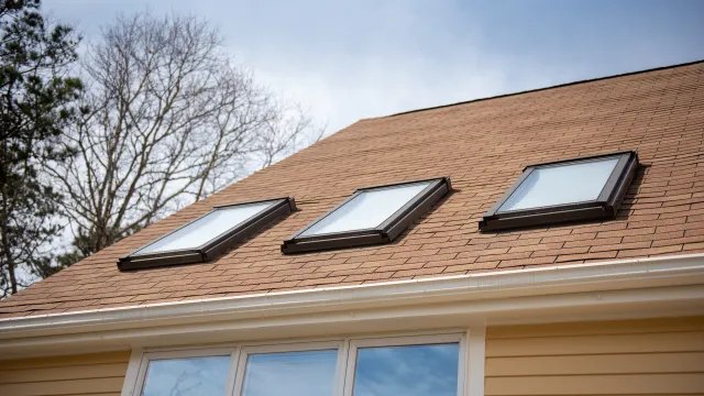 triple skylights on red roof with yellow siding and blue sky with trees in background