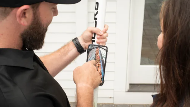 Man showing woman a photo on a phone while holding a white pole outdoors near a house entrance.