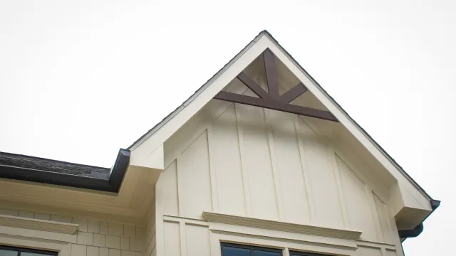 Exterior close-up of a modern beige house with dark-framed windows and a steep gable roof.