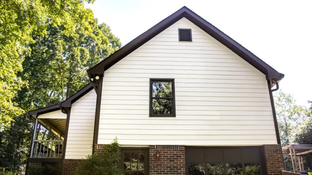 White siding and brick house exterior with a garage, surrounded by green trees under clear sky