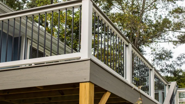 Outdoor deck with wood base and modern metal and white railing surrounded by trees in daylight