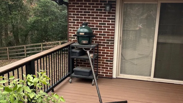 Modern two-story house with grey siding, multiple windows, wooden deck, and outdoor grill area on a sunny day.