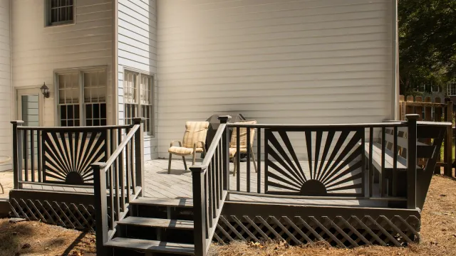 Cozy backyard deck with sunburst railing design, two chairs, and light-colored siding on house exterior.
