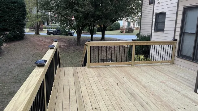 New wooden backyard deck with black metal railing attached to beige house, surrounded by trees and grass.