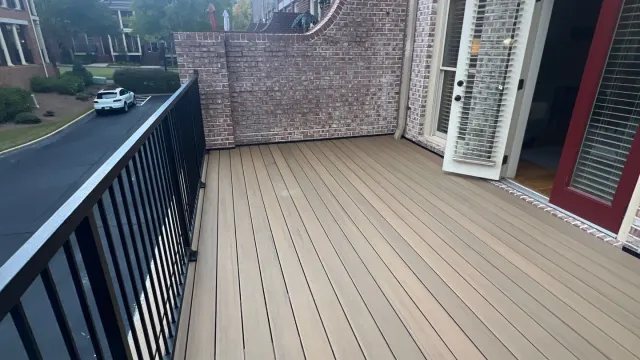 Spacious balcony with light brown decking, black metal railing, and open door to brick building interior.