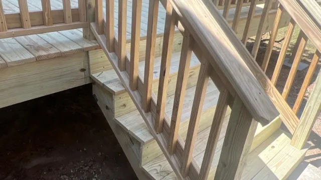 Newly built wooden outdoor deck stair with railing in bright sunlight surrounded by trees.