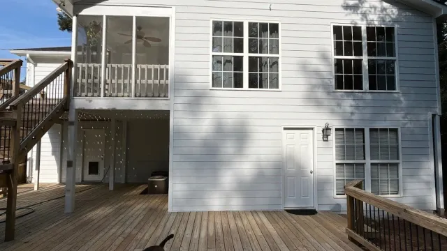 Modern two-story house with grey siding, multiple windows, wooden deck, and outdoor grill area on a sunny day.