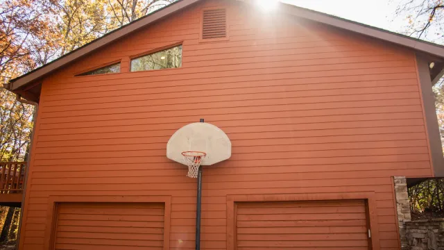 Orange garage with basketball hoop mounted between two large doors and triangular windows near the roof.