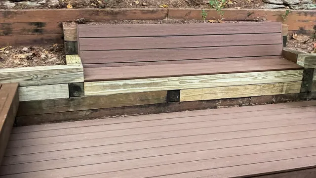 Outdoor wooden bench and deck with greenery and trees in the background in a natural setting.