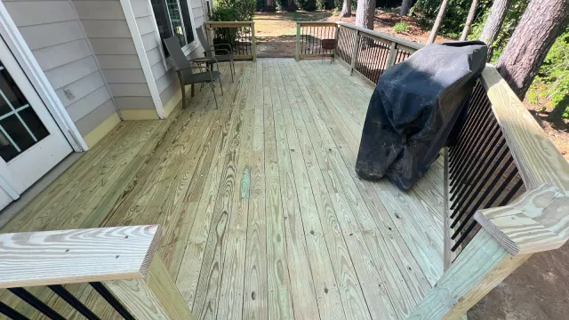 Spacious wooden deck with railing, two chairs, and a covered grill beside a house in a backyard.