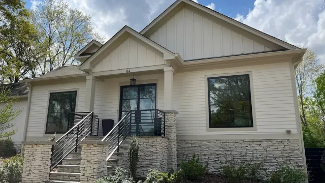 Modern single-story house with white siding, stone accents, black railings, and large windows under a blue sky.
