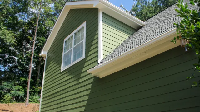Green siding on modern house with white trim and window under clear blue sky with trees background