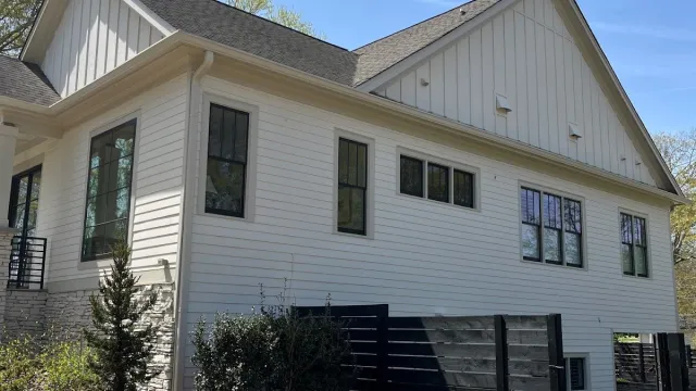 Modern white house with large windows, black fence, neatly landscaped yard, and blue sky overhead.
