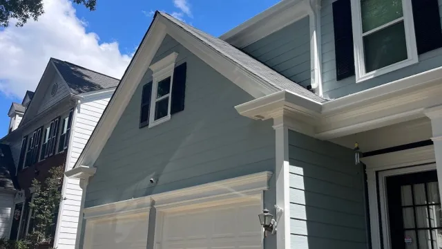 Light blue house with white trim, double garage doors, statue in driveway, and clear blue sky with clouds.