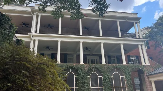 Modern two-story house with grey siding, multiple windows, wooden deck, and outdoor grill area on a sunny day.