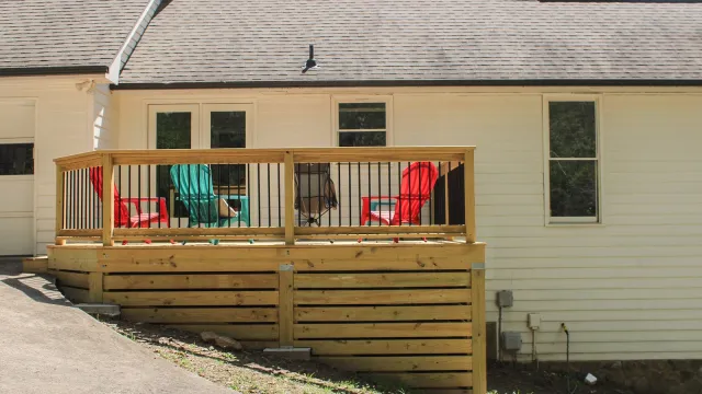 Wooden deck attached to a beige house with red and green outdoor chairs on a sunny day.