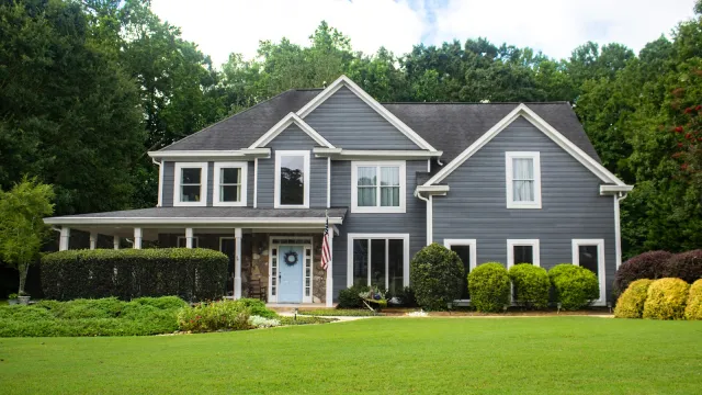 Modern three-story house with large windows and balconies surrounded by lush green trees in a forested area.