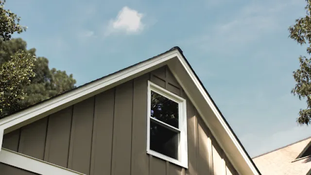 Close-up of a modern house roof and window with clear blue sky and surrounding trees on a sunny day