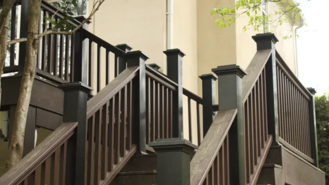 Brown wooden outdoor staircase with black railings surrounded by trees against beige building