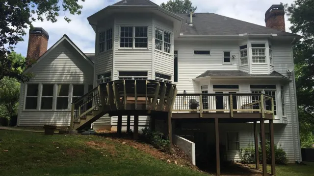 White two-story house with black shutters, glass front door, surrounded by green bushes and tall pine trees.