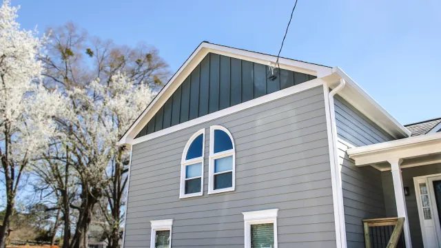 Gray house exterior with white trim and arched window under clear blue sky and blooming trees