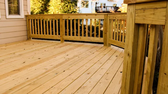 Newly constructed wooden deck with railings next to house under bright sunlight outdoors.